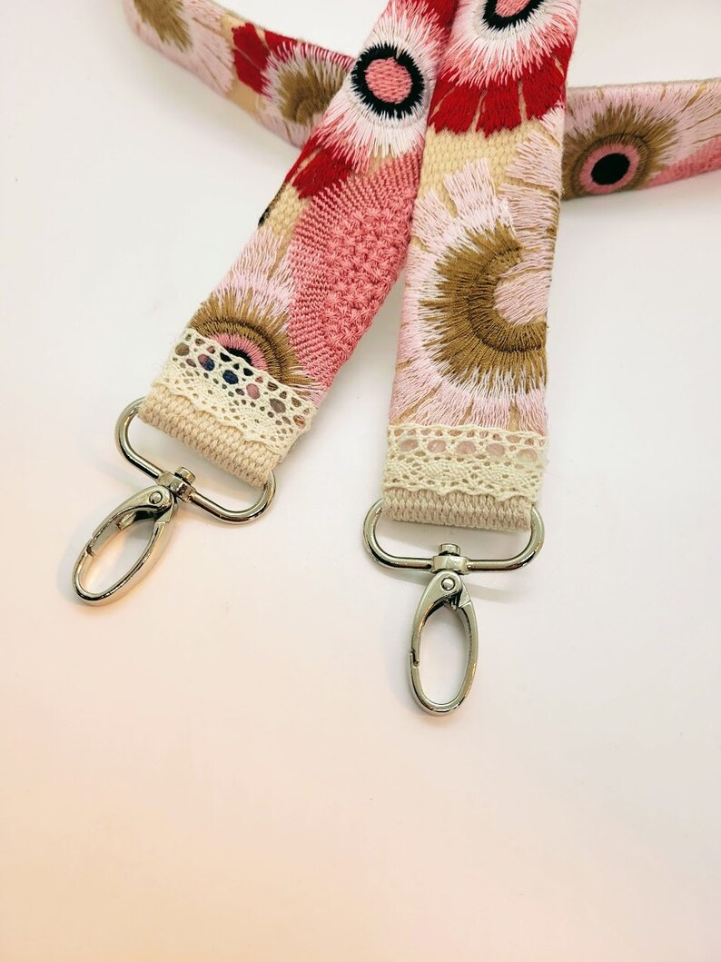 May include: A pink and brown floral fabric strap with white lace trim and silver metal clasps.