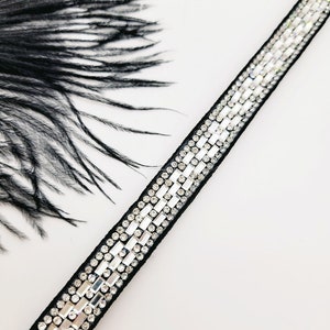 May include: A black ribbon trim with a row of clear rhinestones. The trim is on a white background.