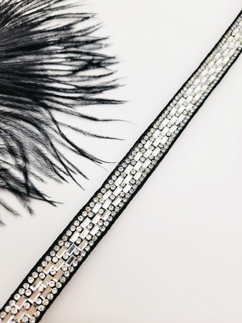May include: A black ribbon trim with a row of clear rhinestones. The trim is on a white background.