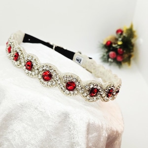 May include: A silver headband with alternating red and clear gemstones. The red gemstones are round and set in a silver bezel, surrounded by smaller clear stones. The headband is on a white surface.