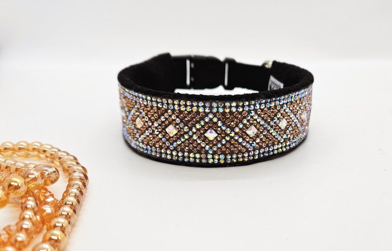 Puede incluir: Un collar de perro negro con un dise&ntilde;o de cristal marr&oacute;n e iridiscente. El collar tiene un patr&oacute;n de diamante con cristales m&aacute;s grandes en el centro de cada diamante.