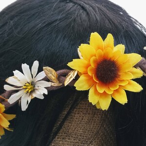 May include: A brown headband with yellow sunflowers and white daisies. The headband is made of fabric and has a rustic look.