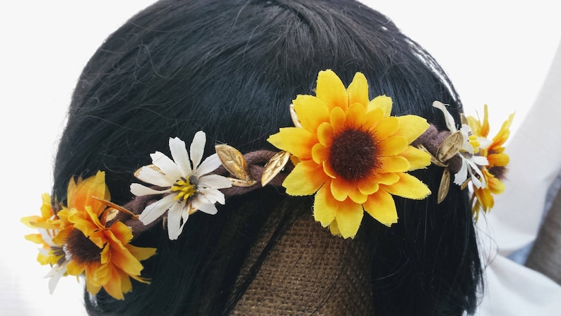 May include: A brown headband with yellow sunflowers and white daisies. The headband is made of fabric and has a rustic look.