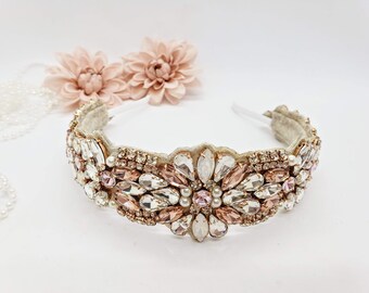Puede incluir: Una diadema dorada con una fila de cristales transparentes y rosados y perlas. La diadema está decorada con un diseño floral.
