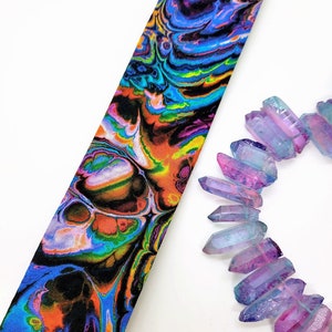 May include: A colorful tie with a swirling, abstract pattern in shades of blue, green, orange, and pink. The tie is made of fabric and has a smooth texture.