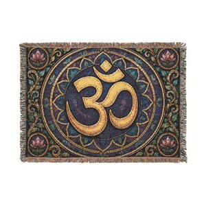 May include: A rectangular woven throw blanket featuring a large gold Om symbol centered within a dark blue circular mandala pattern. The design includes four pink lotus flowers in the corners, intricate floral borders, and fringed edges.