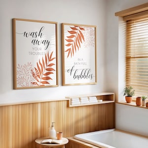 Puede incluir: Dos impresiones enmarcadas con fondo blanco y diseños de hojas marrones y rosas. El texto en las impresiones dice "Wash away your troubles in a bath full of bubbles".