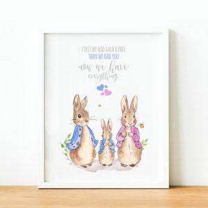 May include: A white framed print with a watercolor illustration of three bunnies. The bunnies are wearing clothes and there are small pink and blue hearts above them. The text reads "First we had each other, then we had you, now we have everything."