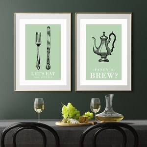 May include: Two framed prints with green backgrounds. The left print features a fork and knife with the text "Let's Eat - Bon Appetit." The right print features a teapot with the text "Fancy a Brew?"