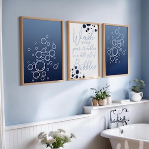 Peut inclure: Trois tableaux encadrés sur le thème de la salle de bain. Deux pièces présentent un fond dégradé bleu foncé avec des illustrations de bulles blanches. La pièce centrale porte le texte "Wash away your troubles in a bath full of Bubbles".