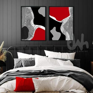 May include: Two black framed abstract art prints featuring white, red, and grey geometric shapes and lines. The prints are hanging on a black wall above a bed with white bedding and a grey throw blanket.