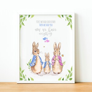 May include: A watercolor illustration of two bunnies with a smaller bunny in the middle. The bunnies are wearing blue and pink jackets. The text reads "First we had each other, then we had you, now we have everything."