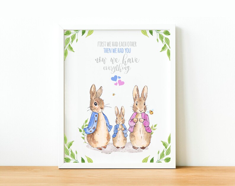 May include: A watercolor illustration of two bunnies with a smaller bunny in the middle. The bunnies are wearing blue and pink jackets. The text reads "First we had each other, then we had you, now we have everything."