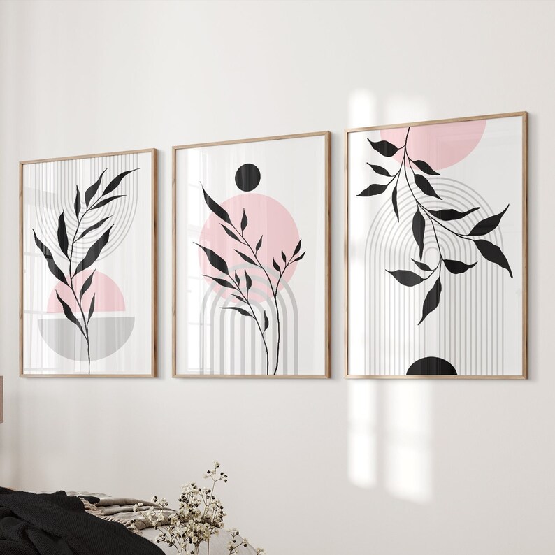May include: Set of three abstract art prints featuring black and white stylized branches with pink and gray geometric shapes. The prints are framed in a light wood frame.