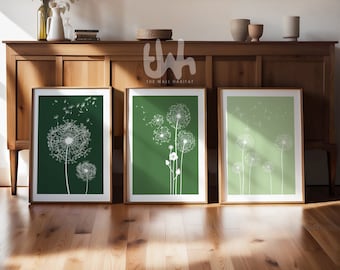 May include: Three framed prints with a green background and white dandelion illustrations. The dandelions are in various stages of blowing away. The prints are on a wooden shelf.