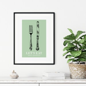 May include: A framed print with a green background featuring a black and white illustration of a fork and knife. The text "LET'S EAT - BON APPETIT" is printed below the illustration.