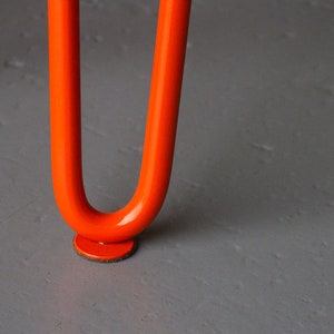 May include: Close-up of an orange metal table leg with a round felt pad on the bottom.