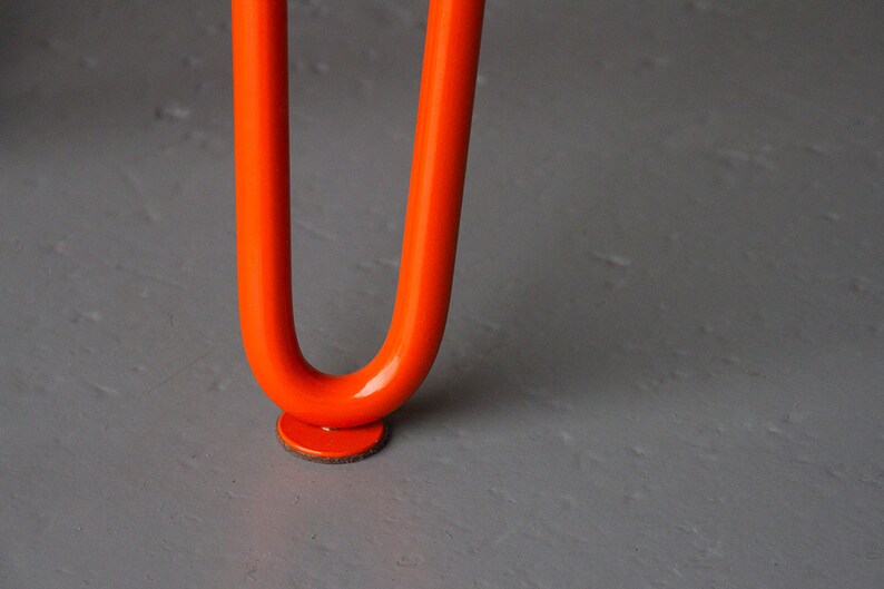 May include: Close-up of an orange metal table leg with a round felt pad on the bottom.