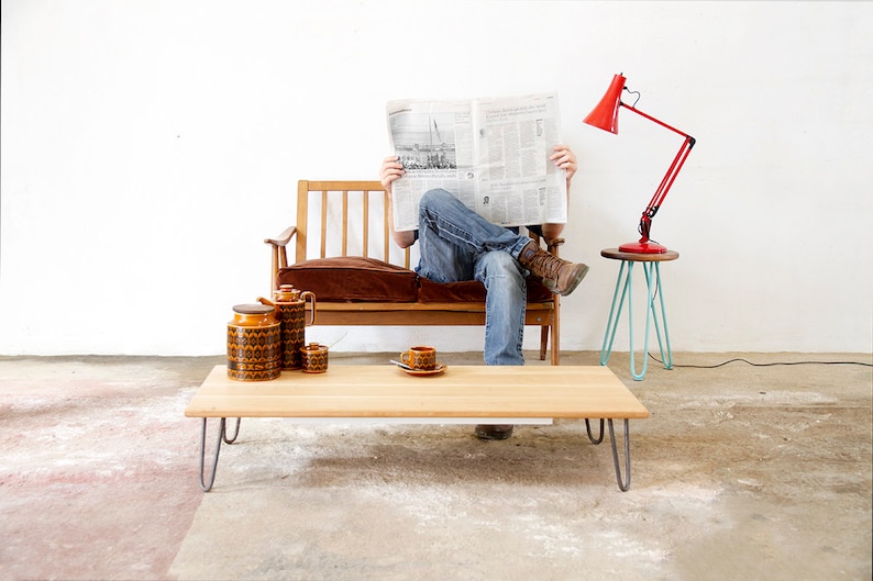 May include: A wooden coffee table with hairpin legs, a brown couch with a brown cushion, and a red lamp on a blue side table. There are three brown ceramic containers on the table.
