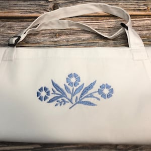 May include: White apron with adjustable straps and a blue embroidered floral design.