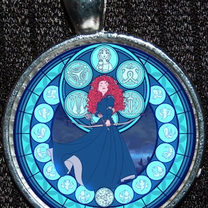 May include: A round, silver pendant with a stained glass design featuring a red-haired woman with a bow and arrow, surrounded by blue and white birds in a circular pattern.