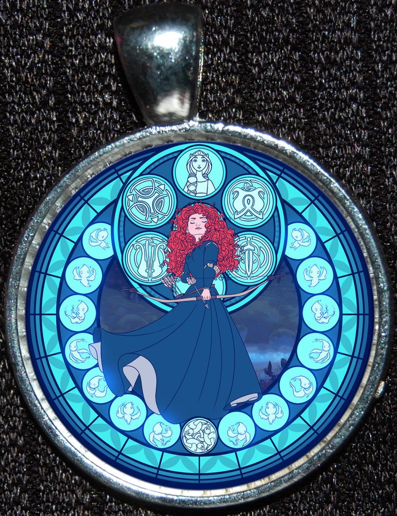 May include: A round, silver pendant with a stained glass design featuring a red-haired woman with a bow and arrow, surrounded by blue and white birds in a circular pattern.