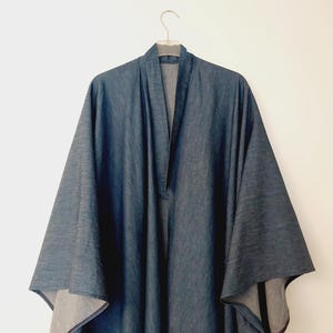 Könnte beinhalten: Ein Kimono aus Denim mit einer langen, fließenden Silhouette. Der Kimono hat einen V-Ausschnitt und lange Ärmel. Der Stoff ist ein dunkelblauer Denim.