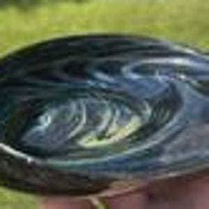 May include: A hand-blown glass bowl with a swirling pattern of dark blue and green. The bowl has a smooth, polished surface and a rounded shape. The bowl is approximately 6 inches in diameter.