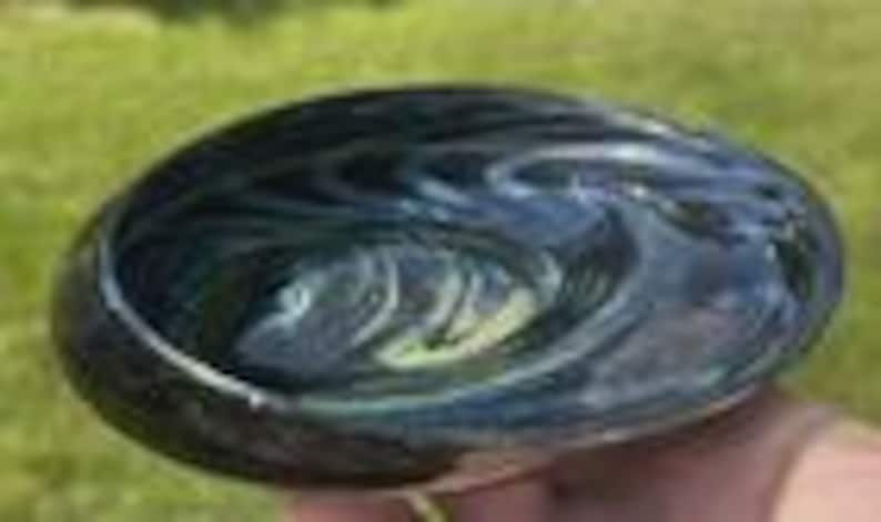May include: A hand-blown glass bowl with a swirling pattern of dark blue and green. The bowl has a smooth, polished surface and a rounded shape. The bowl is approximately 6 inches in diameter.