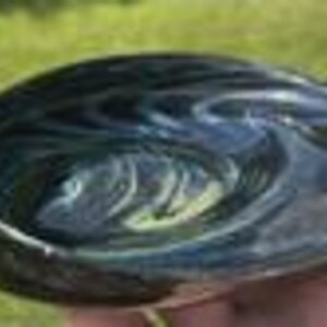 May include: A hand-blown glass bowl with a swirling pattern of dark blue and green. The bowl has a smooth, polished surface and a rounded shape. The bowl is approximately 6 inches in diameter.