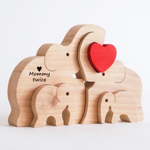 Könnte beinhalten: Holzpuzzle einer Elefantenfamilie mit einem roten Herzen. Der größte Elefant trägt die Worte "Mommy twice" und ein kleines Herz ist in ihn geschnitzt.