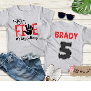 May include: Gray t-shirt with the text "high five" in red and a black handprint. The text "It's my birthday!" is also in red. The back of the shirt has the name "BRADY" in red and the number "5" in black.