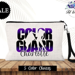 May include: A white canvas cosmetic bag with a black zipper and wrist strap. The bag features the words "COLOR GUARD" in large, purple and black letters, with the name "Charlotte" below. A silhouette of a color guard performer is also visible.