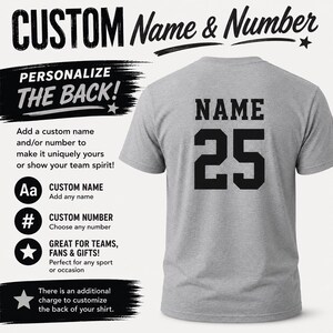 May include: A heather gray short-sleeve t-shirt featuring the black text NAME and the number 25 printed on the back. The image includes text stating CUSTOM Name & Number, PERSONALIZE THE BACK!, and additional details regarding custom name and number options.
