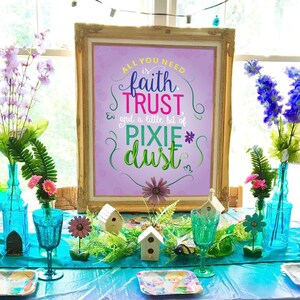Könnte beinhalten: Eine türkisfarbene Tischdecke mit einem Tinkerbell-Muster ist für eine Party gedeckt. Der Tisch ist mit Blumen, Vogelhäusern und einem Schild dekoriert, auf dem steht: "Alles, was du brauchst, ist Glaube, Vertrauen und ein bisschen Feenstaub".