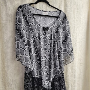 May include: A black and white snakeskin print dress with a black polka dot skirt. The dress has a V-neck and a bow at the neckline. The dress is made of a sheer fabric.