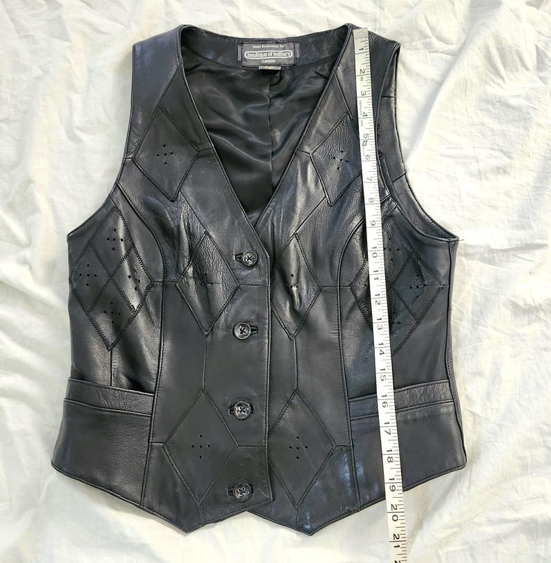 Puede incluir: Chaleco de cuero negro con cuello en V, dise&ntilde;o de patchwork en forma de diamante y cierre de botones. El chaleco tiene dos bolsillos delanteros y mide aproximadamente 53 cm de largo.
