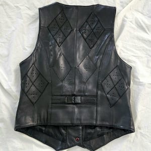 Puede incluir: Chaleco de cuero negro con detalles en forma de diamante y perforaciones. El chaleco tiene cierre de bot&oacute;n y un corte entallado. La parte trasera del chaleco es visible, mostrando las intrincadas costuras y el dise&ntilde;o. Una prenda de vestir cl&aacute;sica.