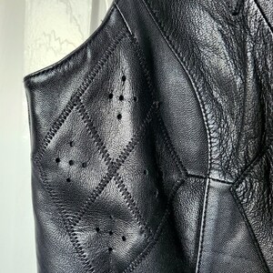 Puede incluir: Primer plano de un chaleco de cuero negro con un patr&oacute;n de costuras en forma de diamante. El chaleco tiene peque&ntilde;as perforaciones espaciadas uniformemente y costuras visibles. El cuero parece texturizado y el chaleco es sin mangas.