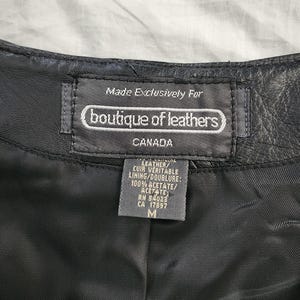 Puede incluir: Primer plano de una etiqueta de prenda de cuero negro. La etiqueta dice "Made Exclusively For boutique of leathers CANADA". La etiqueta tambi&eacute;n enumera los materiales como cuero y 100% acetato. La talla es M.