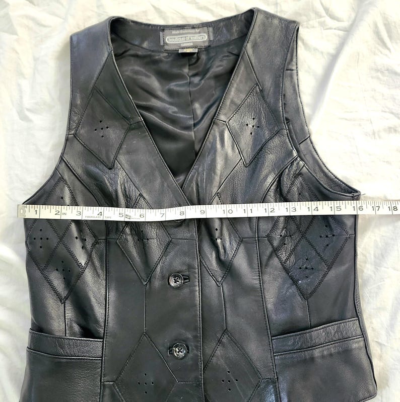 Puede incluir: Chaleco de cuero negro con cuello en V y dise&ntilde;o de patchwork en forma de diamante. El chaleco tiene dos bolsillos y tres botones en la parte delantera. El chaleco mide aproximadamente 43 cm de ancho.