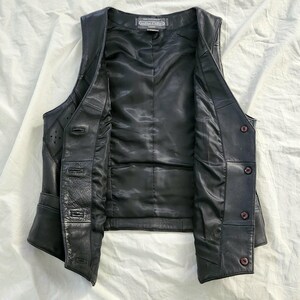 Puede incluir: Chaleco de cuero negro con cierre de botones y forro de sat&eacute;n. El chaleco tiene un dise&ntilde;o cl&aacute;sico con un corte entallado, costuras decorativas y detalles sutiles. El chaleco est&aacute; abierto, mostrando el forro interior y los cierres de bot&oacute;n.