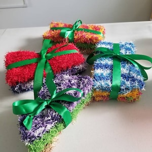 May include: Four sets of colorful crocheted dishcloths tied with green ribbon. The dishcloths are in shades of red, yellow, blue, and purple.