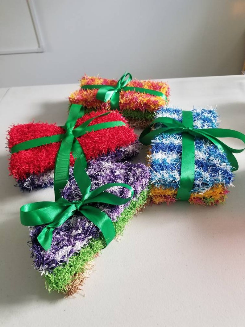 May include: Four sets of colorful crocheted dishcloths tied with green ribbon. The dishcloths are in shades of red, yellow, blue, and purple.