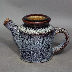 May include: A ceramic teapot with a speckled blue, brown, and white glaze. The teapot has a spout, a handle, and a circular opening at the top. The rim of the opening and the spout's tip are a darker brown.