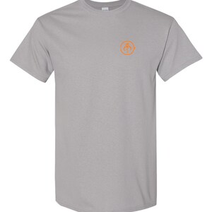 May include: A gray t-shirt with a small orange circle on the front. The circle contains a stylized graphic of a spider.