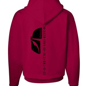 Puede incluir: Una sudadera con capucha color granate con una silueta negra de un casco mandaloriano y el texto "This is the way" escrito verticalmente en la espalda.