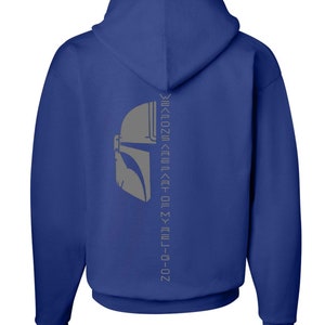 Puede incluir: Una sudadera con capucha azul real con un gr&aacute;fico de casco mandaloriano gris y el texto "This is the way" en una fuente vertical invertida en la parte posterior.