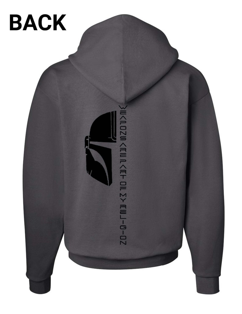 Puede incluir: Una sudadera con capucha gris oscuro con una silueta negra de un casco mandaloriano en la espalda. El texto "This is the way" est&aacute; escrito en escritura mandaloriana en la parte posterior de la sudadera.