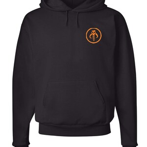 Puede incluir: Sudadera con capucha negra con un s&iacute;mbolo mandaloriano naranja en la parte delantera.